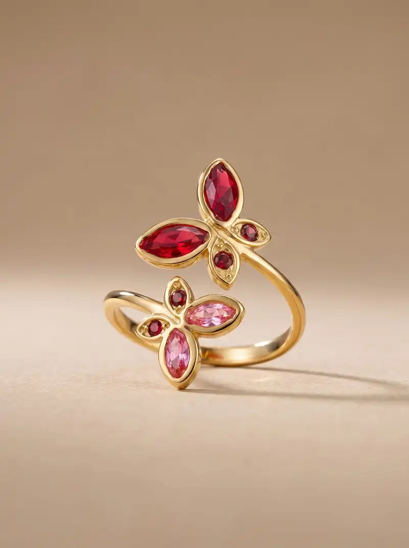 Goudkleurige verstelbare Berry Butterfly ring van stainless steel met twee vlindervormige details en roze en rode steentjes.