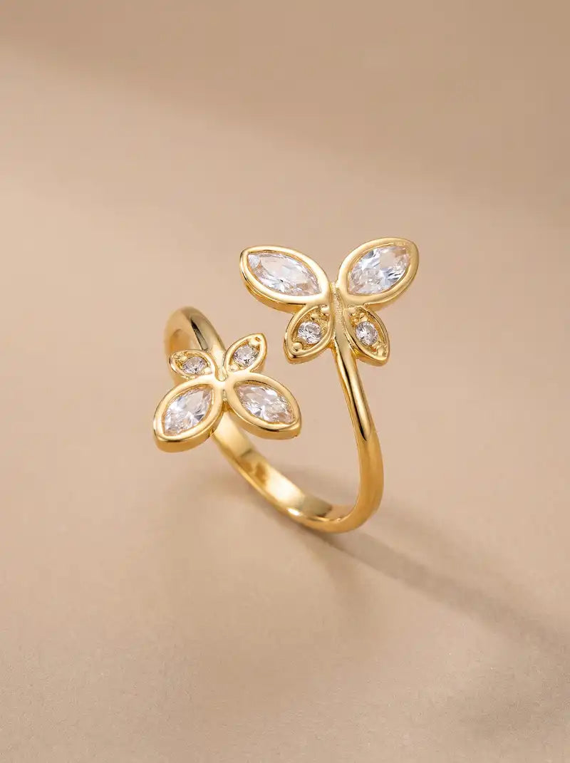 Goudkleurige verstelbare Butterfly Kisses ring van stainless steel met twee vlindervormige details en transparante steentjes.